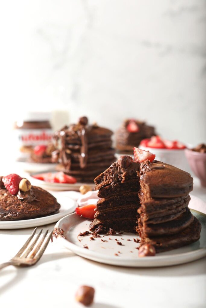 Four stacks of chocolate pancakes on plates, garnished with strawberries