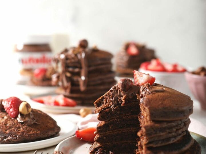 Four stacks of chocolate pancakes on plates, garnished with strawberries