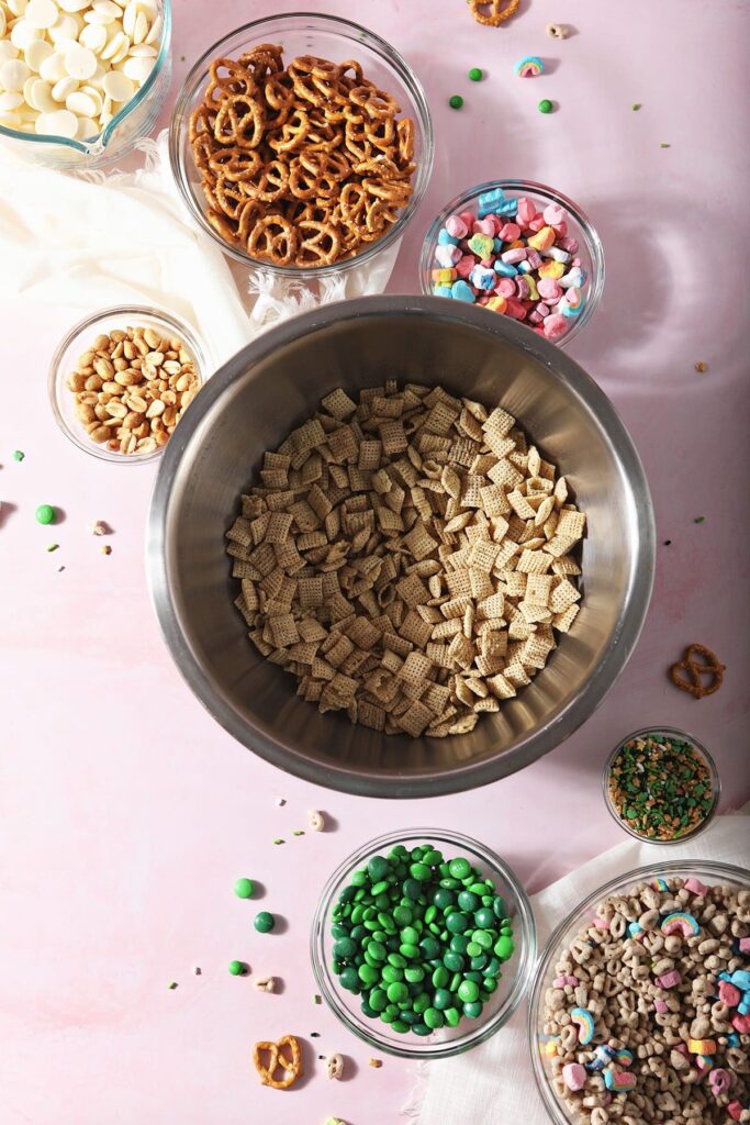 Ingredients for a St. Patrick's Day Snack Mix in bowls on a pink countertop