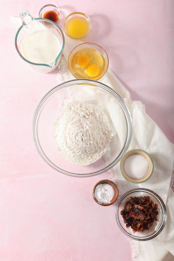 Ingredients to make bacon pancakes in bowls on a pink surface