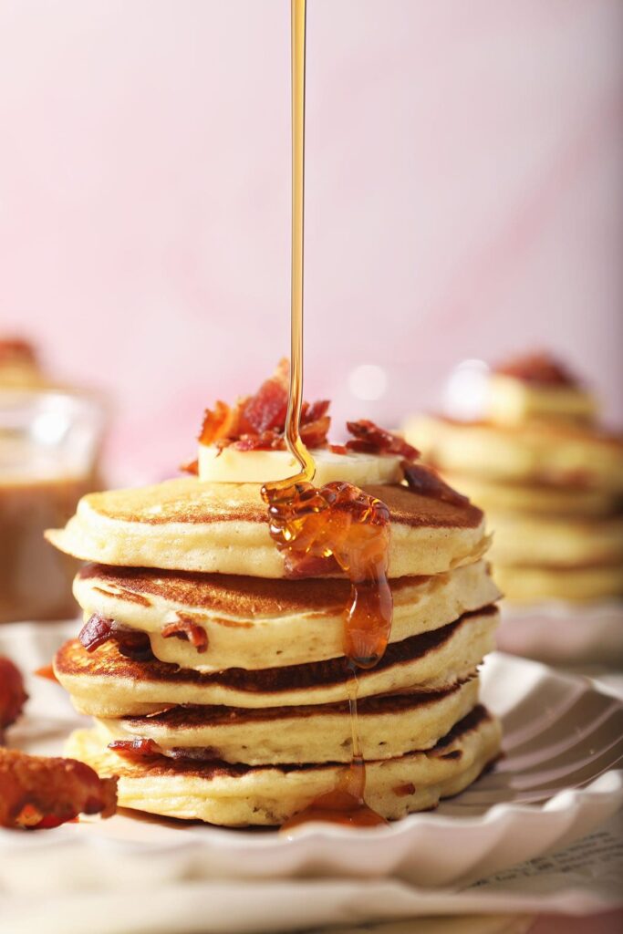 Syrup pours onto a stack of bacon pancakes