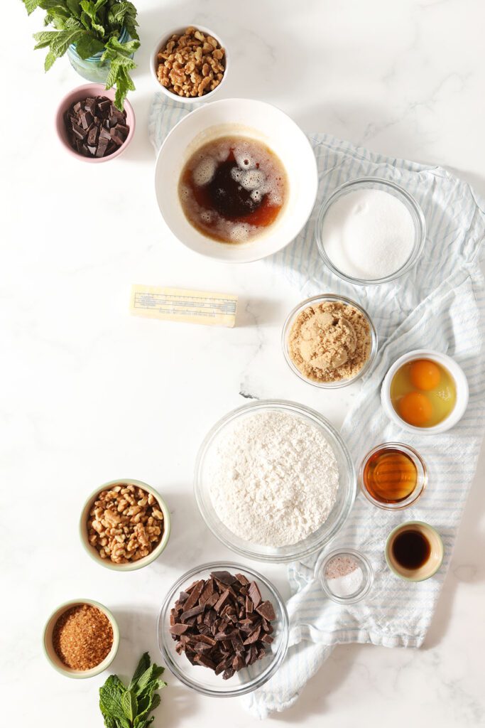 Ingredients to make chocolate chip cookies in bowls on marble