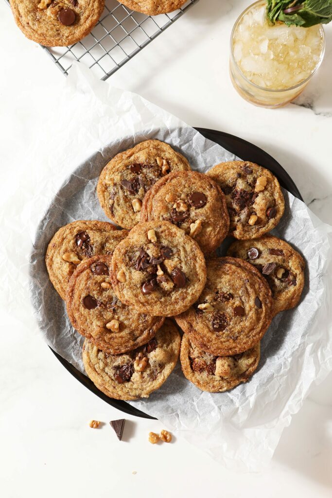 A plate of brown butter chocolate chip cookies next to a glass of bourbon