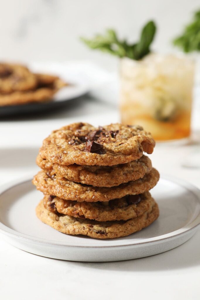 Brown Butter Bourbon Chocolate Chip Cookies stacked on top of each other on a plate with a julep in the background