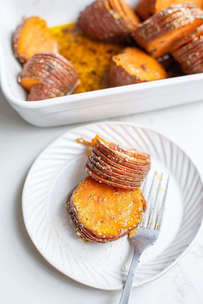 A portion of a hasselback sweet potato on a white plate with a fork