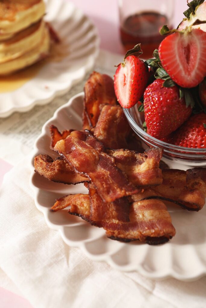 Cooked bacon on a plate next to sliced strawberries