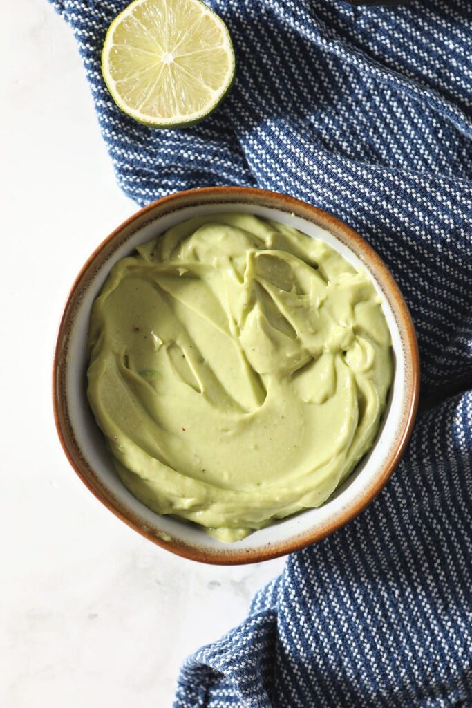 A bowl of avocado sauce from above on marble with a blue towel