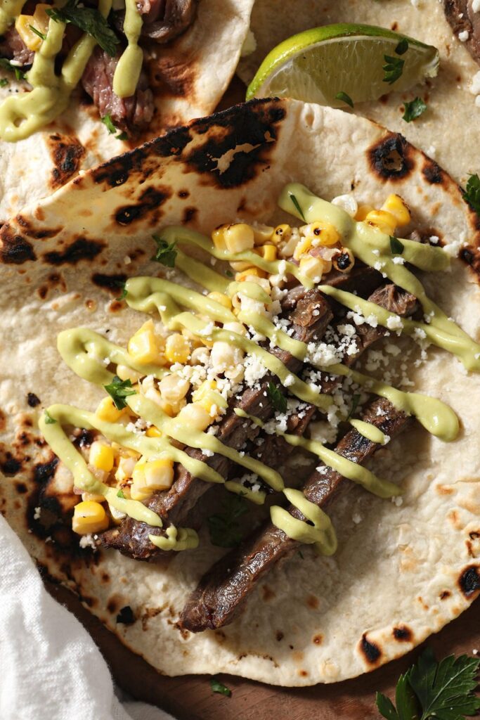 A steak taco with corn salsa and an avocado cream drizzled on top