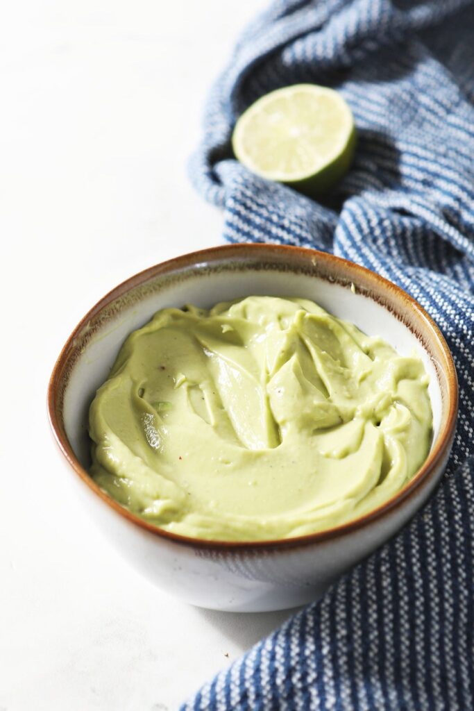 A bowl of Avocado Cream Sauce on marble with a blue towel