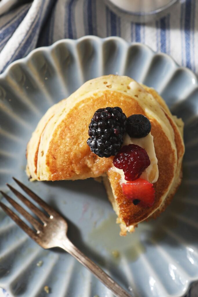 A cut-into stack of buttermilk pancakes from above with berries and butter on top