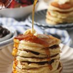 Maple syrup pours on top of a stack of homemade buttermilk pancakes
