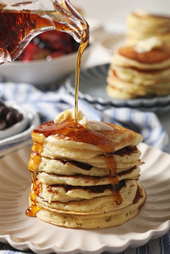 Maple syrup pours on top of a stack of homemade buttermilk pancakes