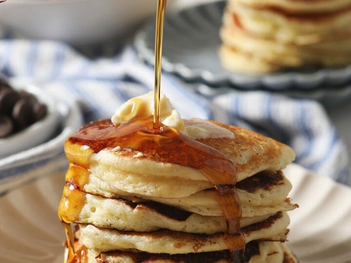 Maple syrup pours on top of a stack of homemade buttermilk pancakes
