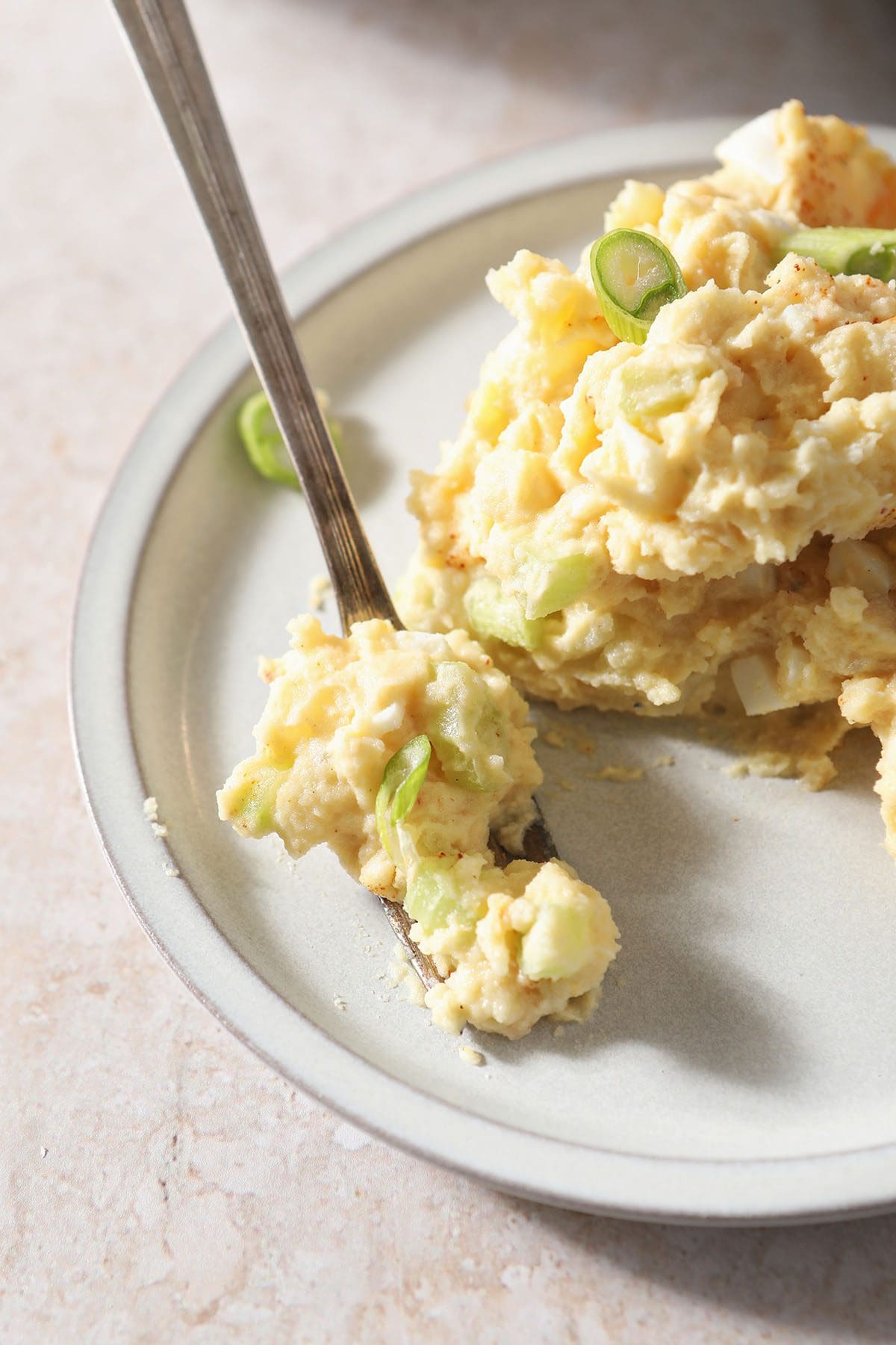 Potato salad on a plate with a fork garnished with green onions