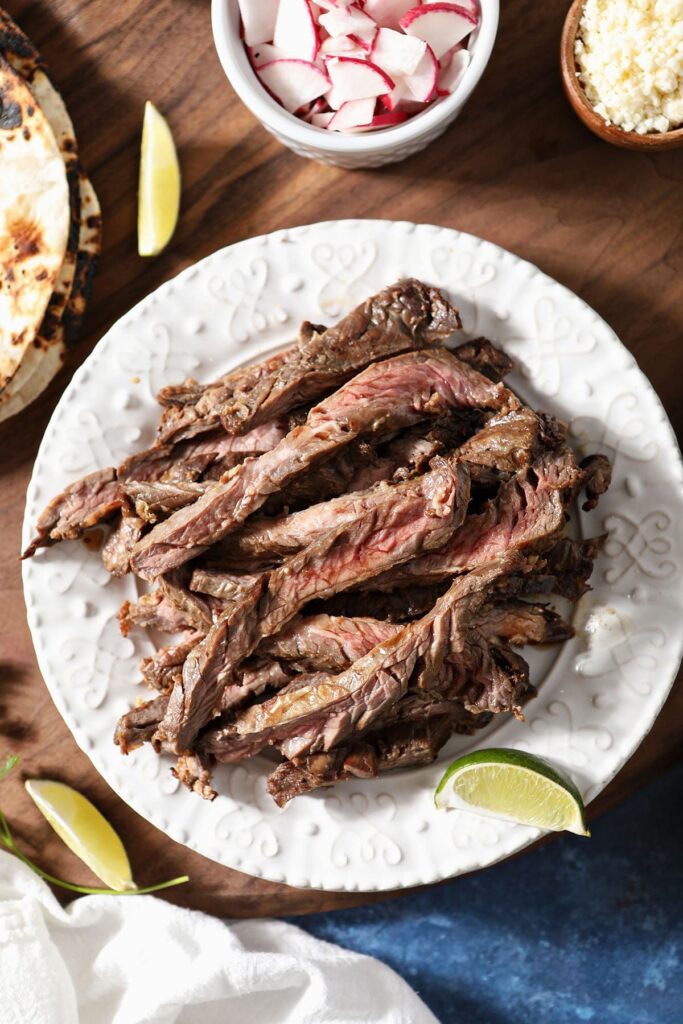 Sliced skirt steak on a plate surrounded by taco toppings