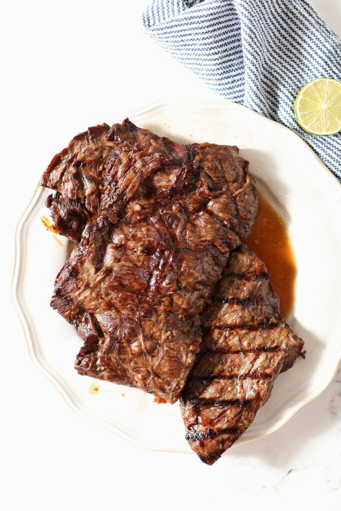 Two grilled skirt steaks on a white plate before cutting