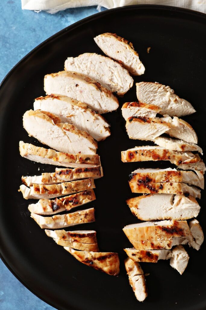 Two sliced marinated and grilled chicken breasts on a black plate