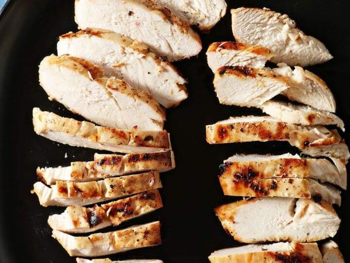 Two sliced marinated and grilled chicken breasts on a black plate