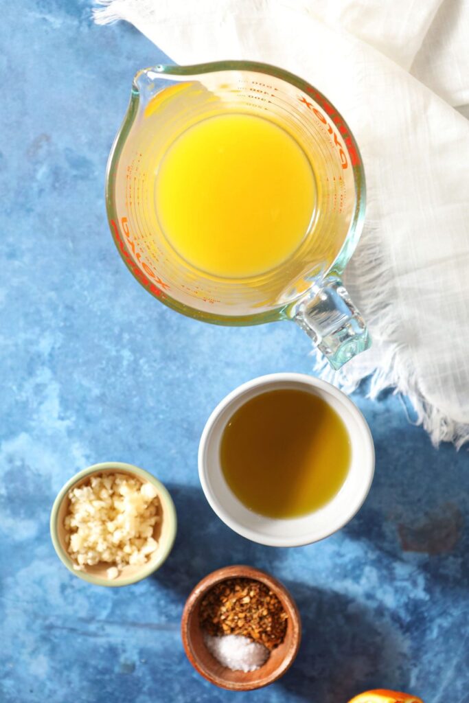 Orange juice and other marinade ingredients in bowls on a blue countertop