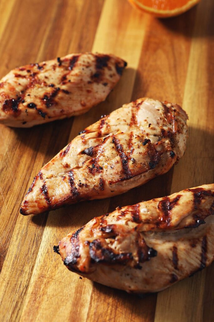 Three grilled chicken breasts on a wooden cutting before before slicing