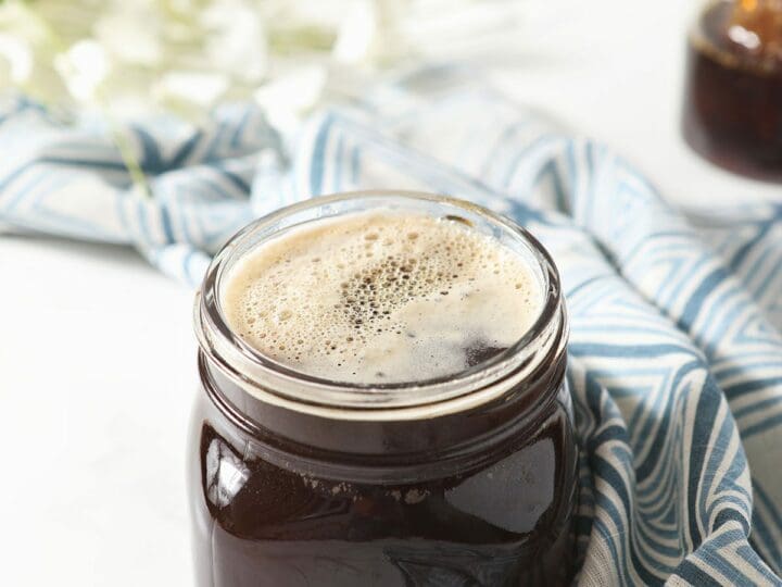 A jar of honey simple syrup on marble next to a geometric blue towel and flowers