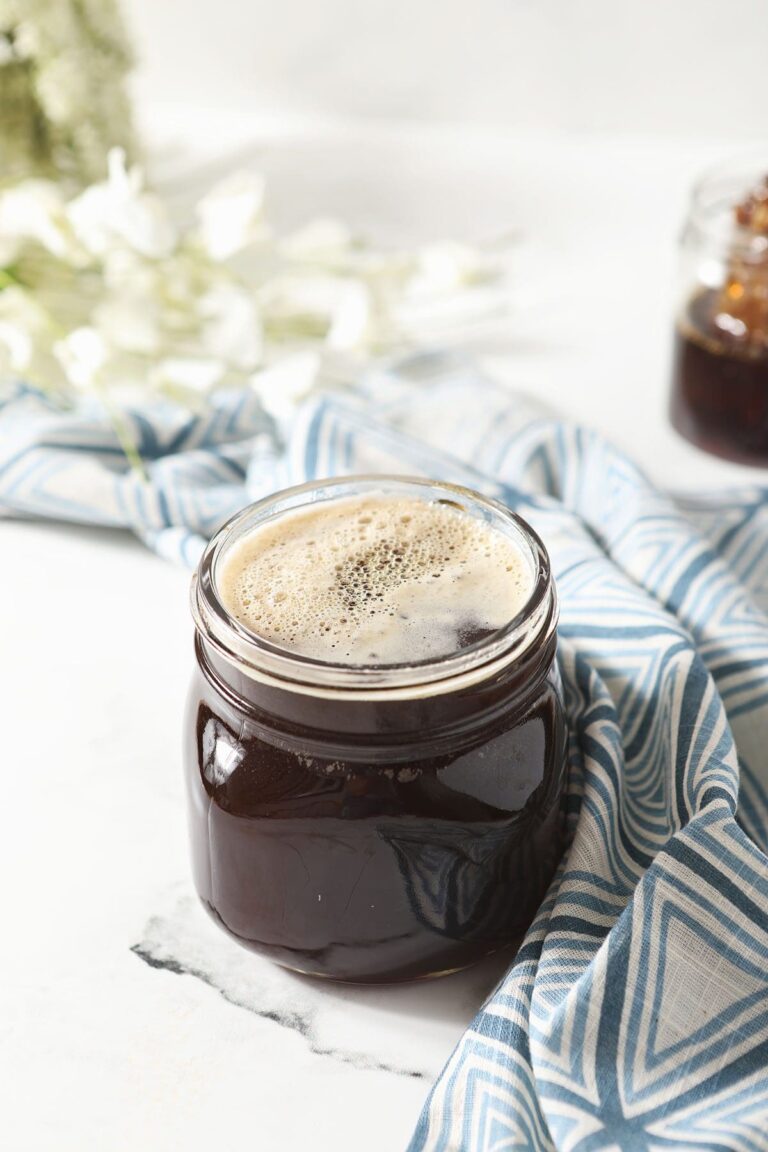 A jar of honey simple syrup on marble next to a geometric blue towel and flowers