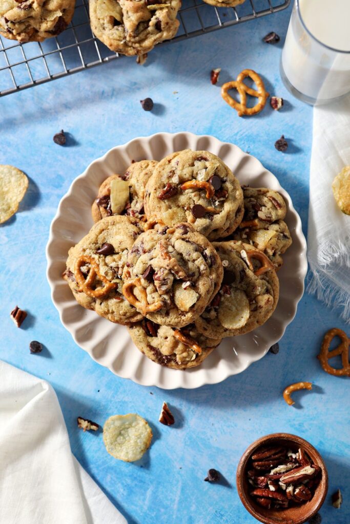 A plate of baked Kitchen Sink Cookies next to a cooling rack on a blue counter