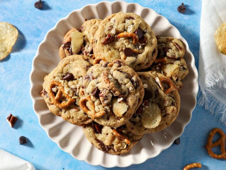 A plate of baked Kitchen Sink Cookies next to a cooling rack on a blue counter