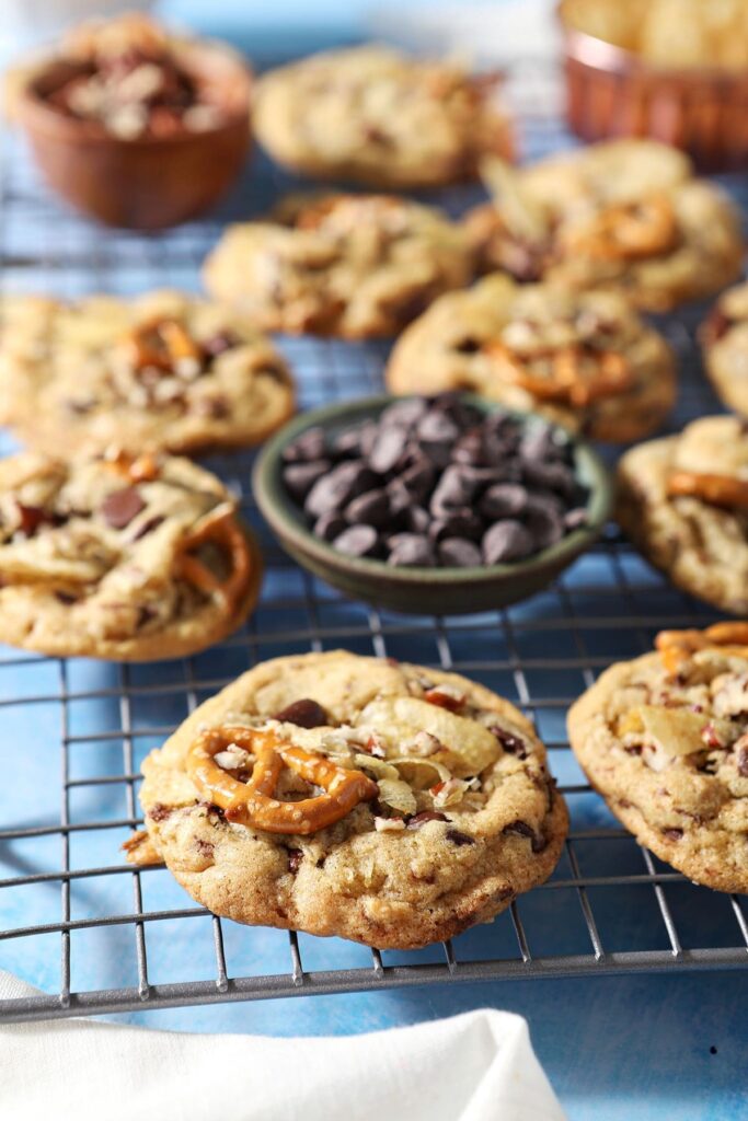 Kitchen Sink Cookies cool on a wire rack next to a bowl of chocolate chips