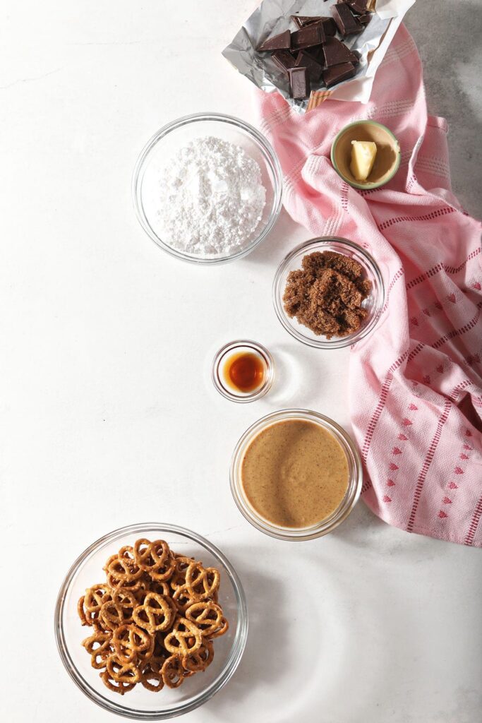 Ingredients to make chocolate-dipped peanut butter pretzels in bowls on marble