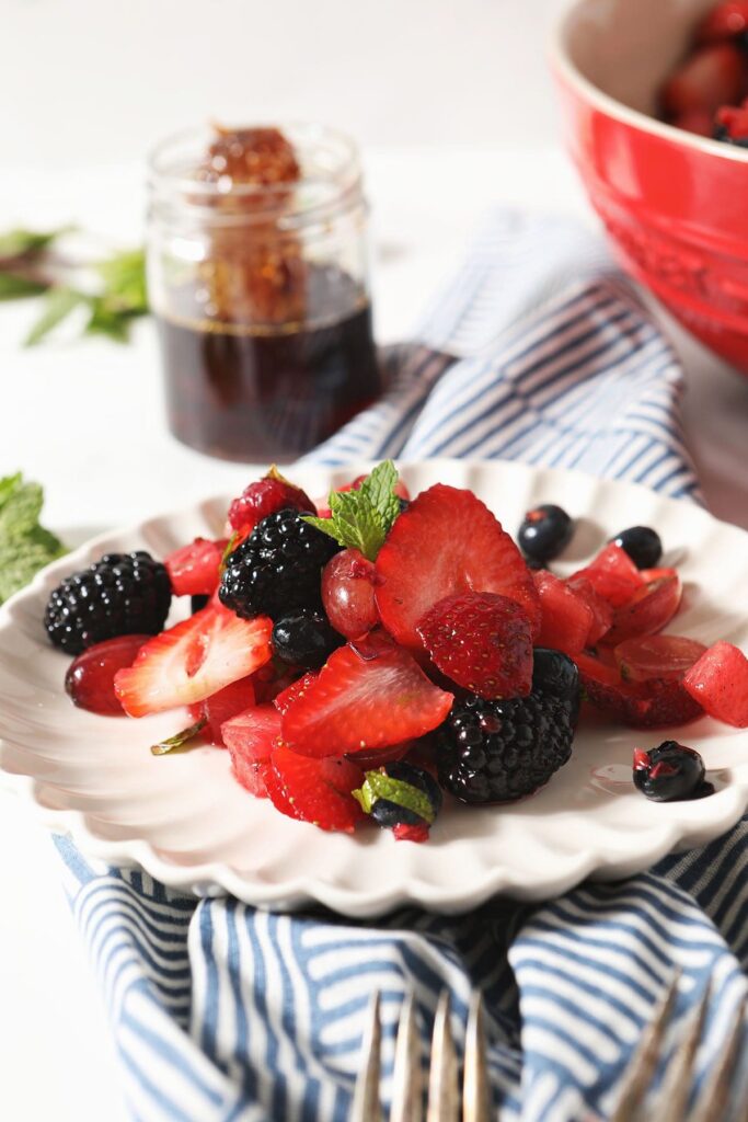 A plate of berry fruit salad with watermelon in front of a jar of honey