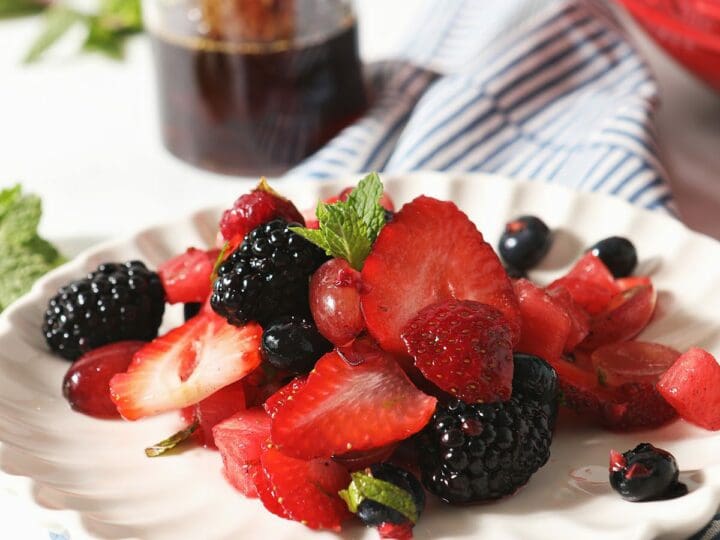 A plate of berry fruit salad with watermelon in front of a jar of honey