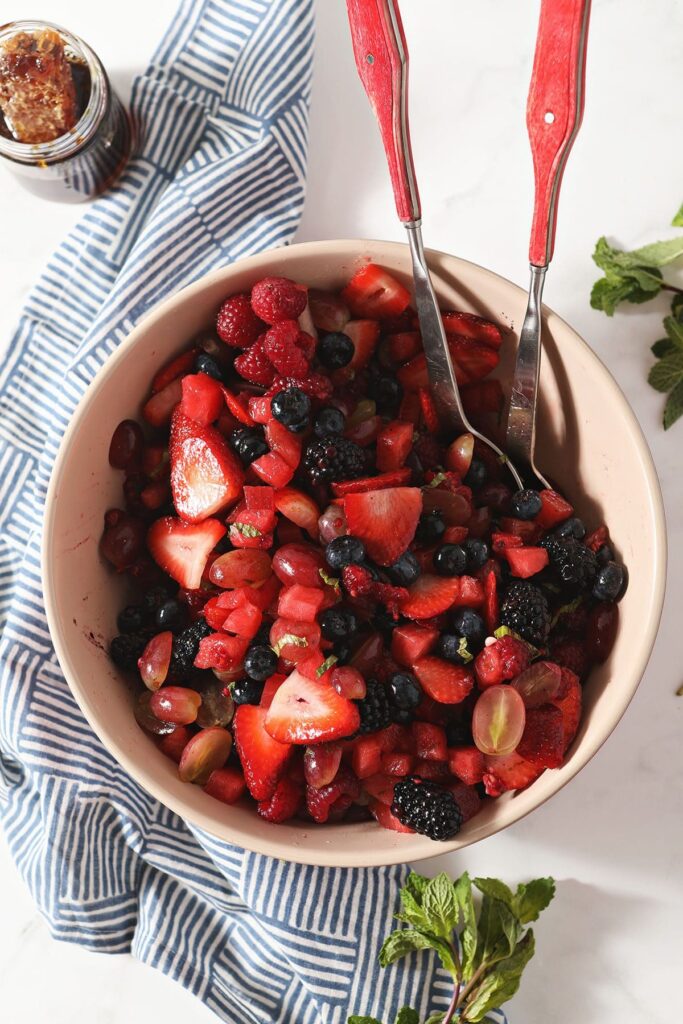 A bowl of Summer Fruit Salad with serving tongs next to a geometric towel