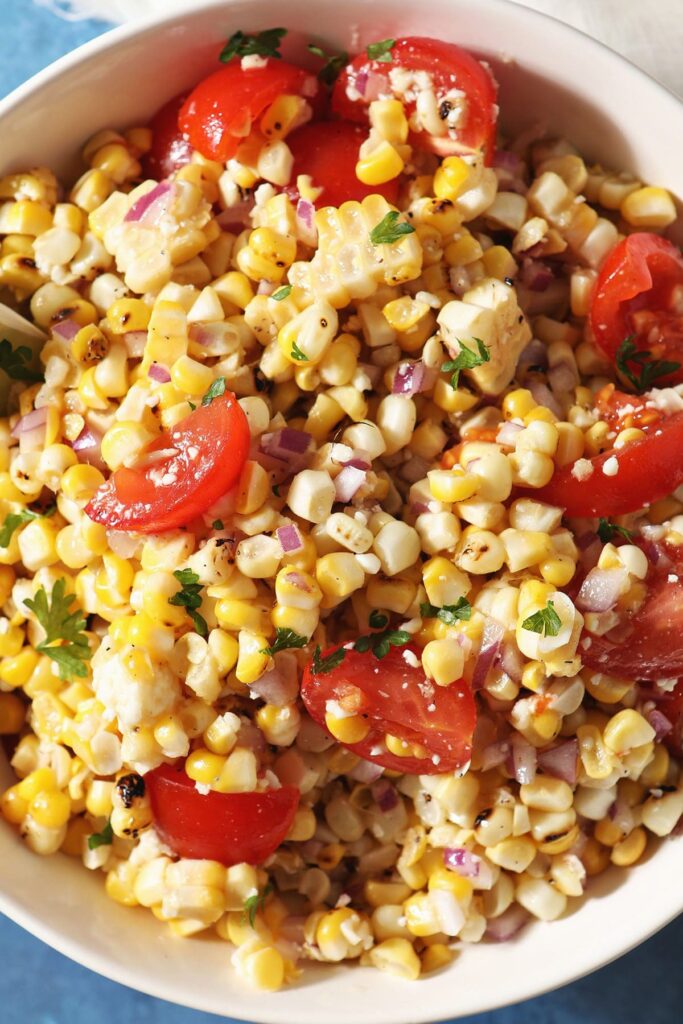 Close up of Grilled Corn Salsa in a bowl with tomatoes, limes and parsley