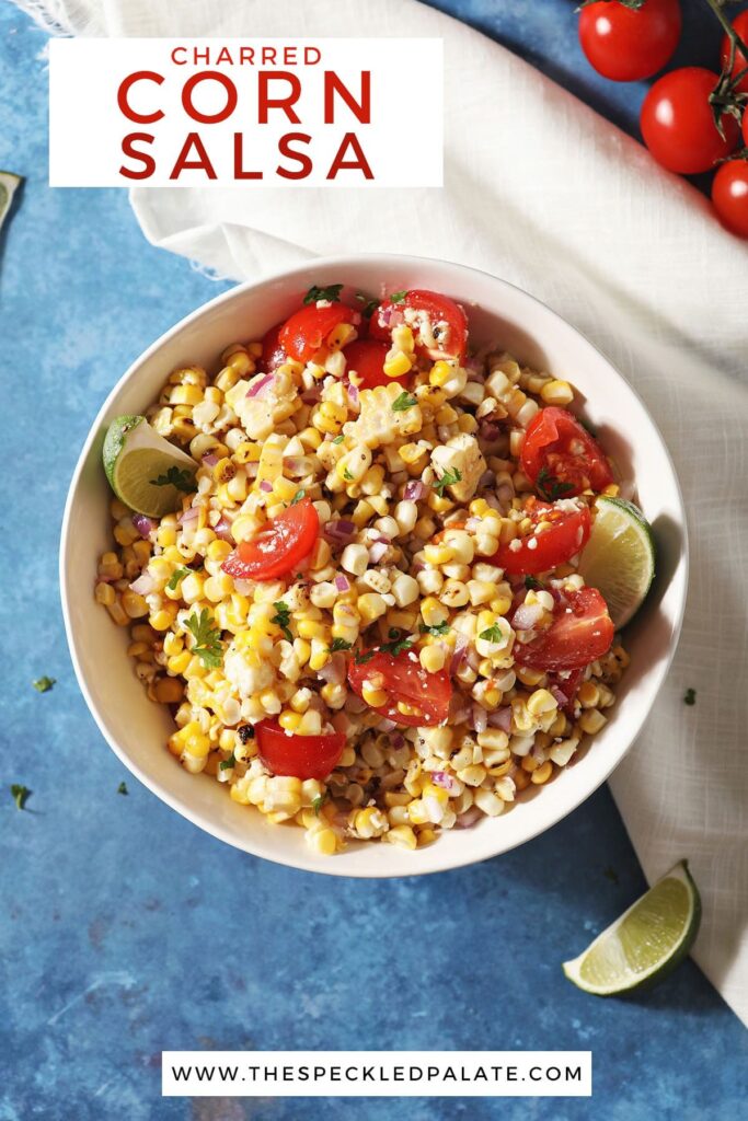 A bowl of corn salsa with tomatoes and limes on a blue countertop with the text charred corn salsa