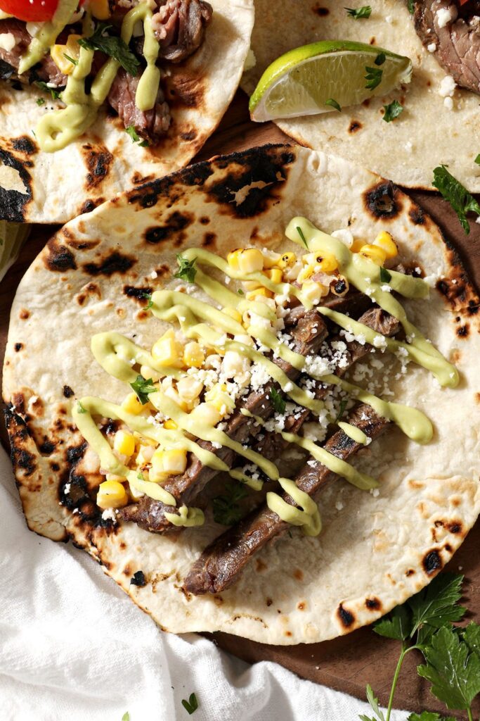 Close up of a skirt steak taco with corn salsa and an avocado cream sauce on wood