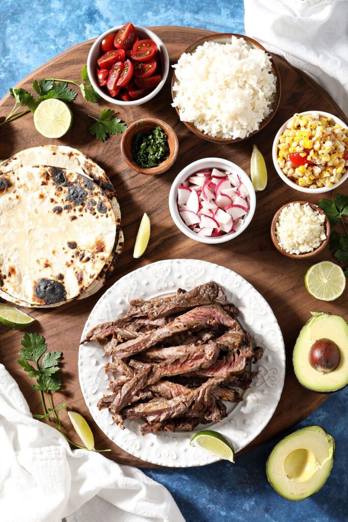 Ingredients to make steak tacos on a wooden cutting board in bowls