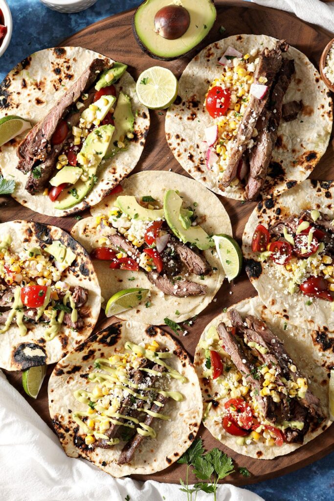 Seven skirt steak tacos dressed on a wooden board before eating