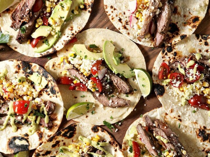 Seven skirt steak tacos dressed on a wooden board before eating