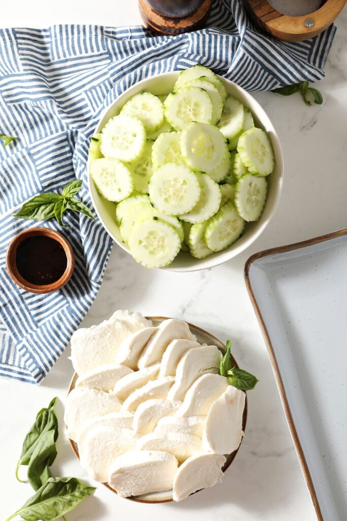 Ingredients for cucumber capers salad in bowls on marble with a blue patterned napkin