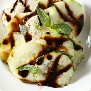 A serving of caprese salad with cucumbers on a white plate