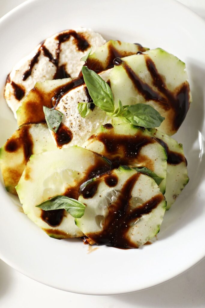 A serving of caprese salad with cucumbers on a white plate