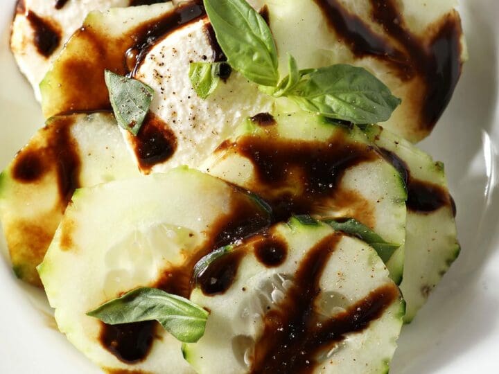 A serving of caprese salad with cucumbers on a white plate