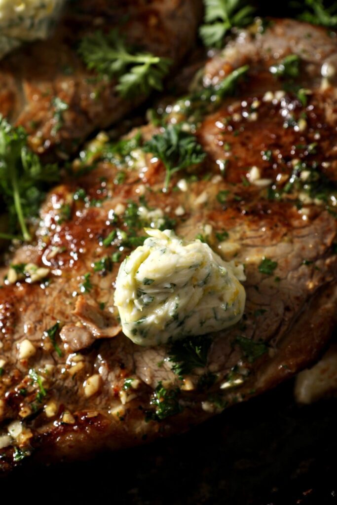 Close up of a scoop of garlic herb butter for steak on top of a steak