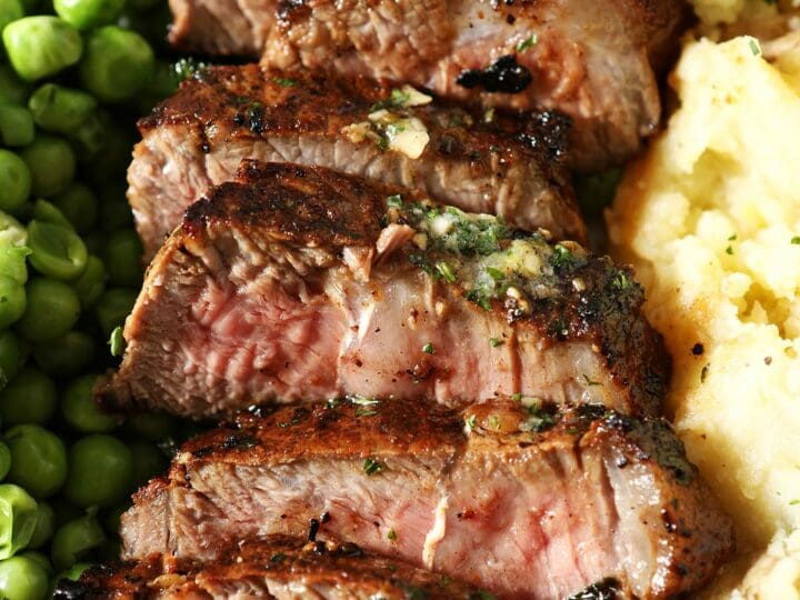 Close up of sliced garlic butter steak on a plate with peas and mashed potatoes