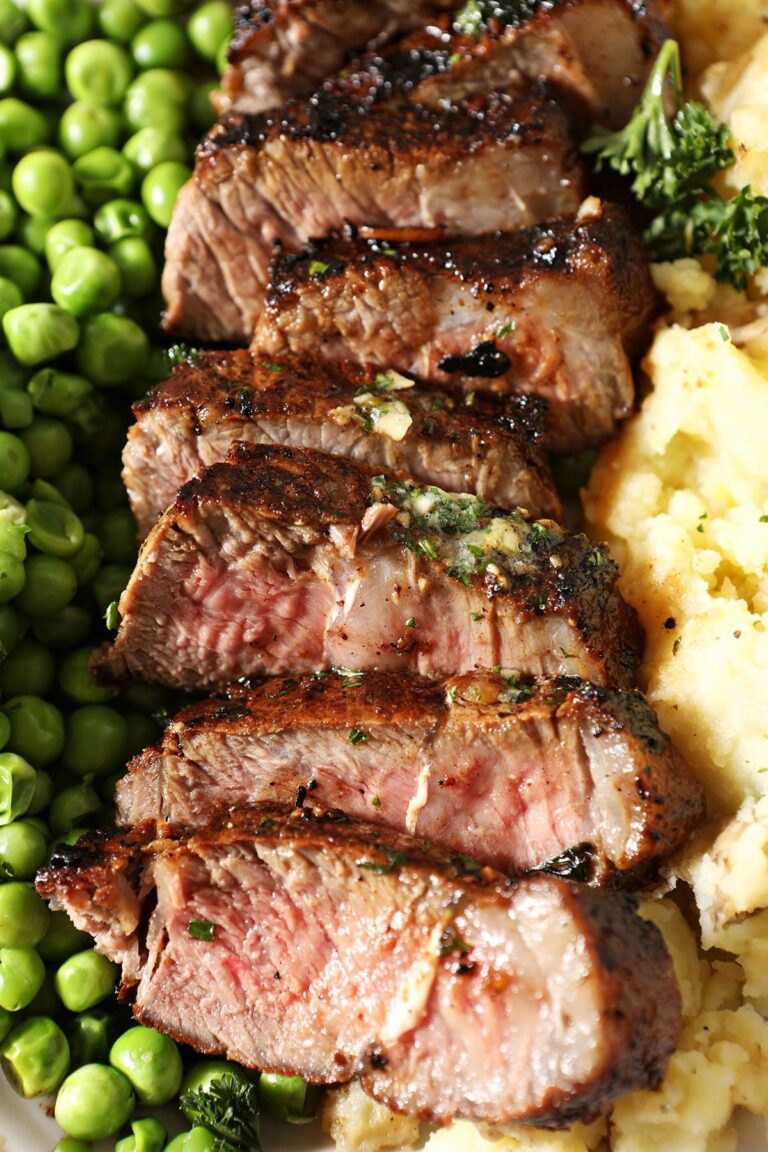 Close up of sliced garlic butter steak on a plate with peas and mashed potatoes