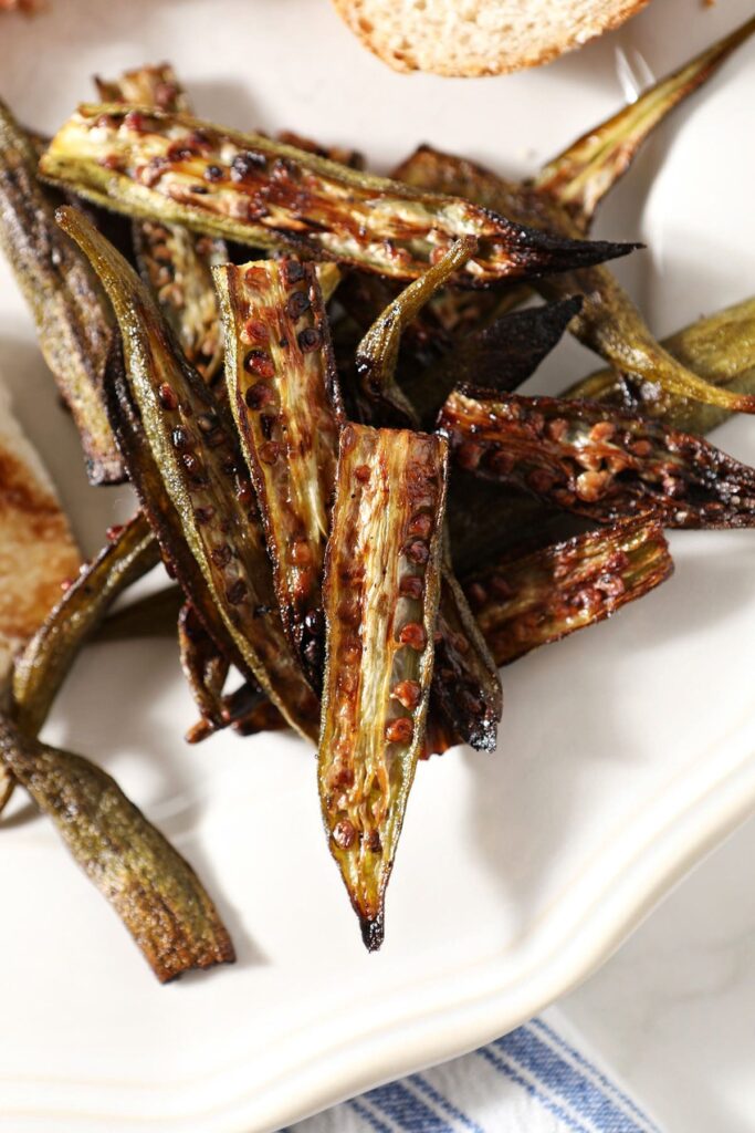 Roast okra on a white plate next to bread and other dishes