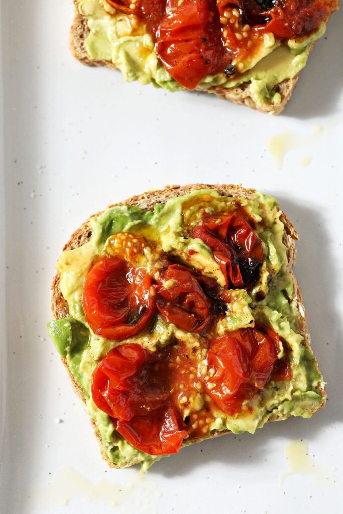 Smashed roasted tomatoes on top of avocado toast on a white plate