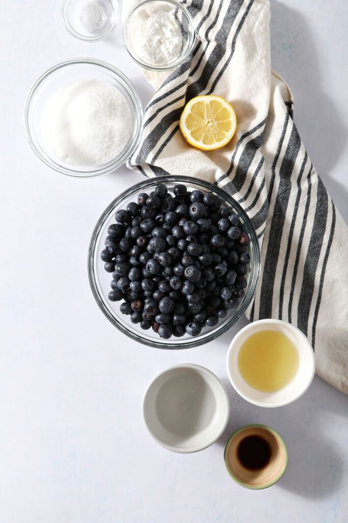 Ingredients to make a homemade blueberry sauce in bowls on a blueish backdrop