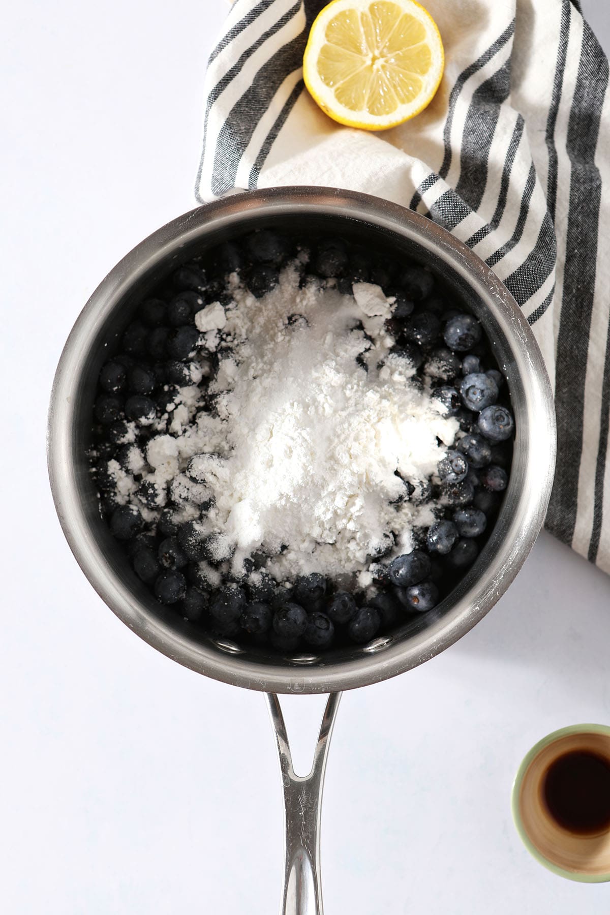ingredients to make a blueberry sauce in a saucepan on a neutral surface with a linen